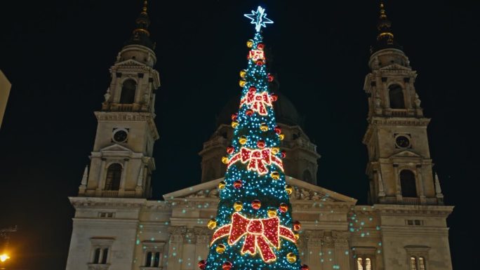 在匈牙利布达佩斯的夜晚，手持低角度拍摄圣斯蒂芬大教堂外装饰的圣诞树