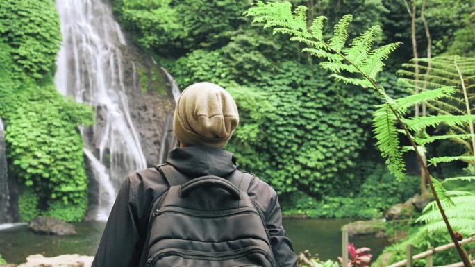 成年男子在绿色大自然中旅行到森林瀑布。一个不知名的年轻人走到丛林瀑布的旅行目的地。《天堂岛之旅》中个