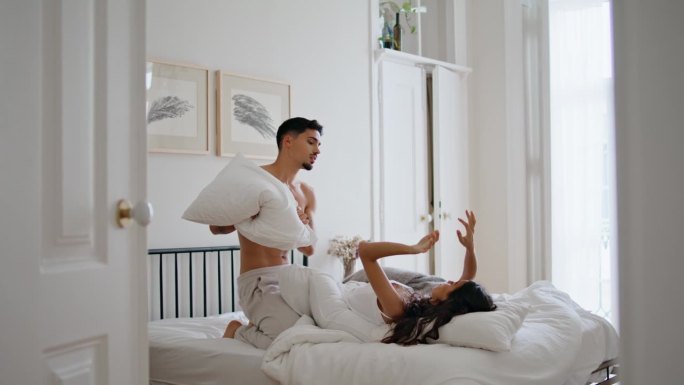 性感男人在舒适的公寓里玩枕头。快乐的夫妻一起打靠垫