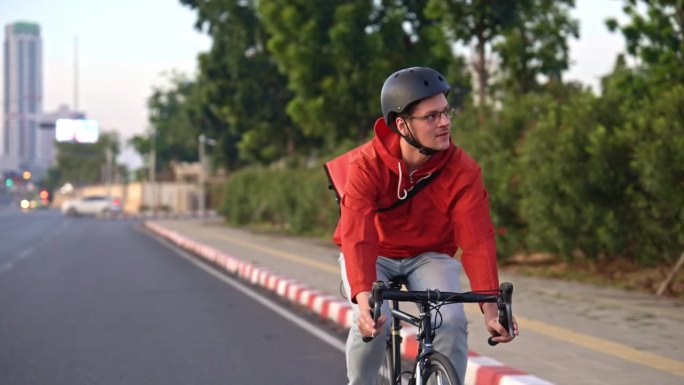 背着红色背包的年轻快递员骑着自行车在城市的街道上送外卖。