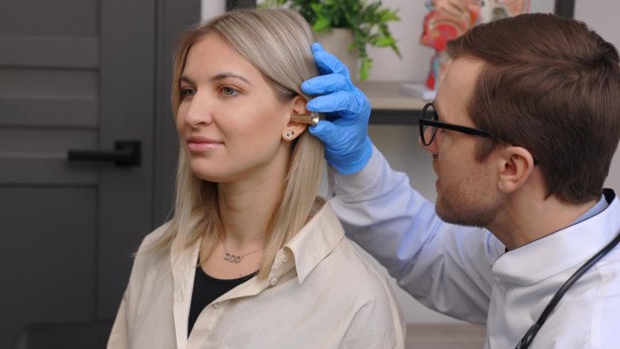 耳鼻喉科医生在耳鼻喉科诊所用耳镜或听诊器检查年轻女子的耳朵。听力考试