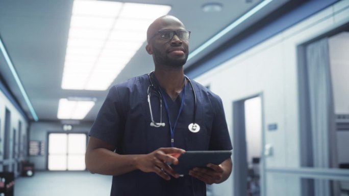 一名态度积极的男医生，平静地走过医院走廊，使用数码平板电脑，向护士和同事打招呼。明亮现代新诊所