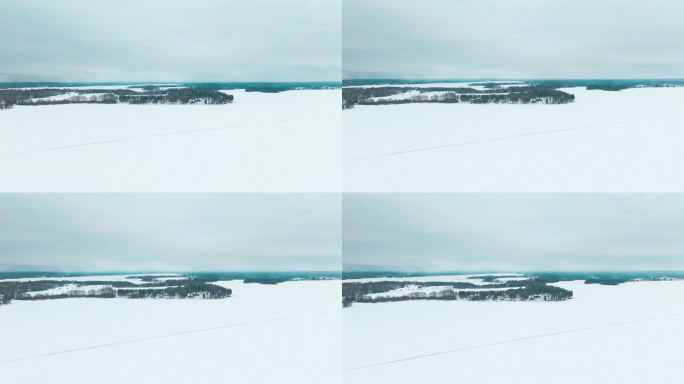 飞越结冰的湖面上的道路，展现雪林的景观。池塘、湖泊和树林一直延伸到地平线。Tammela,芬兰。阴天
