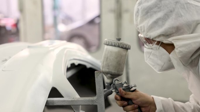 在专业车库的汽车重漆服务室，穿着白色PPE制服和面罩的4K高加索人在下一道工序前喷涂白色，中年男性技