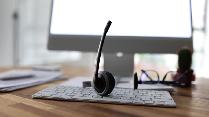 呼叫中心话务员头戴式耳机、眼镜、键盘和支持服务员工工作场所的显示器