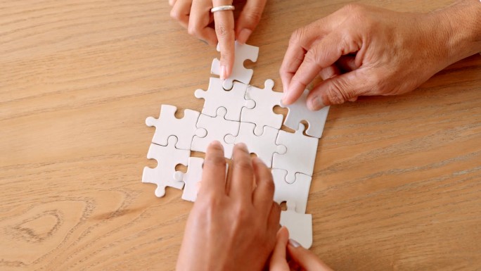 不同的人的手一起合作，把拼图拼在一起。把桌子上的东西连接起来，找到一个共同的目标。顶部特写视图与复制