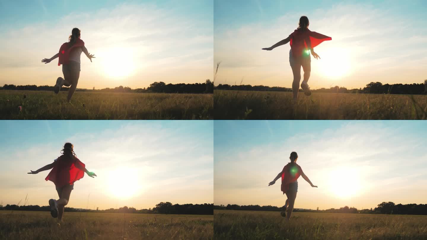女孩扮演超级英雄。快乐的女孩在玩超级英雄。日落时分，孩子们穿着红斗篷跑过绿色的田野。在大自然中穿着红