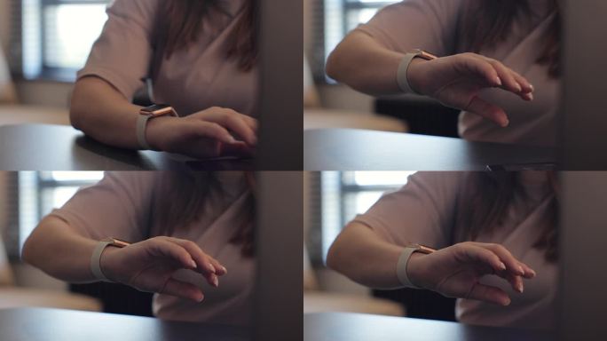 女性手指可以双击智能手表，实现免提交互。年轻女子正在办公室的工作桌旁用笔记本电脑打字。