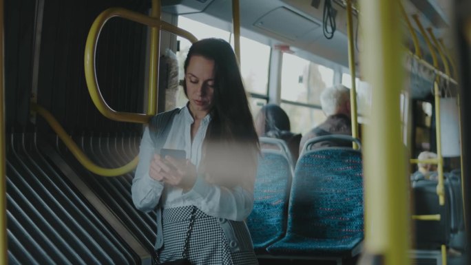 美丽的年轻女子站在城市公交车上，看着手机屏幕，慢动作