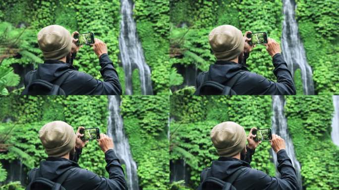 在绿色大自然中旅行的成年男子用手机拍下了森林瀑布。在丛林瀑布旅行目的地的年轻人的生活方式。旅行者制作