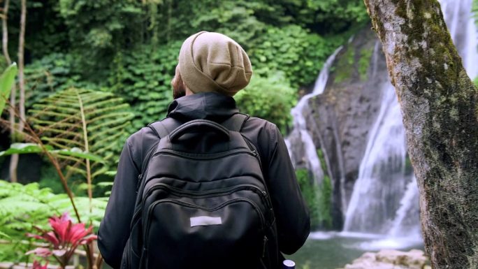 成年男子在绿色自然中前往森林瀑布。一个不知名的年轻人走到丛林瀑布的旅行目的地。天堂岛之旅个人旅行的生
