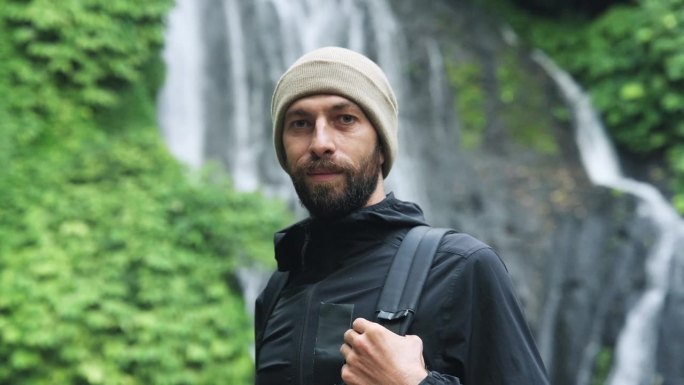 在森林瀑布的绿色自然中看相机的旅行者肖像特写。年轻人在丛林瀑布旅游目的地的生活方式。旅行者天堂之旅的