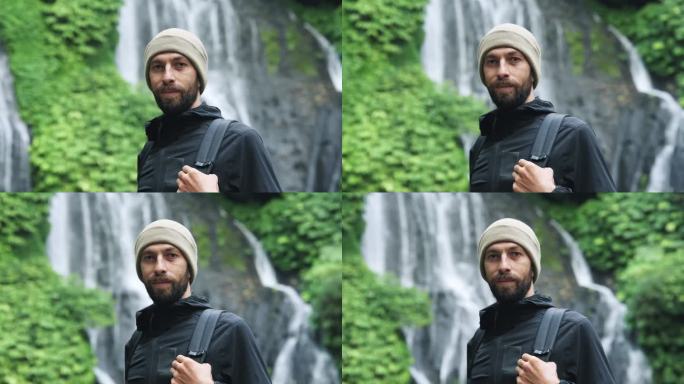 在森林瀑布的绿色自然中看相机的旅行者肖像特写。年轻人在丛林瀑布旅游目的地的生活方式。旅行者天堂之旅的