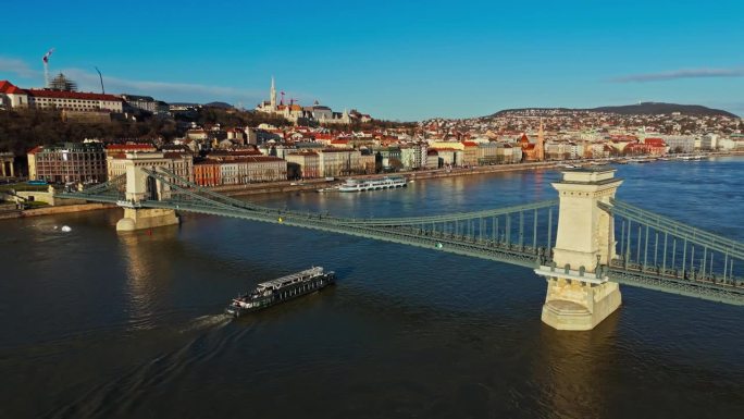 匈牙利布达佩斯，在晴朗的蓝天下，多瑙河Széchenyi链桥下渡船行驶的无人机镜头