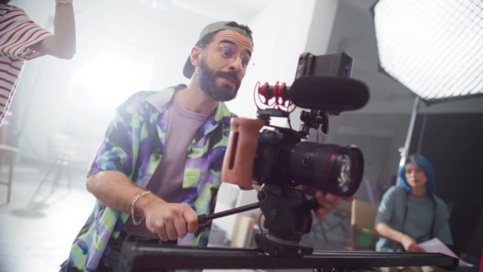 年轻的摄像师在片场工作的肖像，给拍摄的模特指示。男性电影摄影师操作先进的数码相机捕捉高质量的镜头。慢