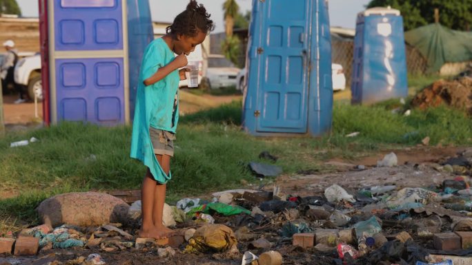 贫穷，贫穷，一个非洲黑人孩子在一个非正式定居点的移动厕所和臭气熏天的污水旁刷牙