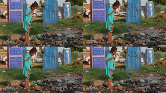 贫穷，贫穷，一个非洲黑人孩子在一个非正式定居点的移动厕所和臭气熏天的污水旁刷牙
