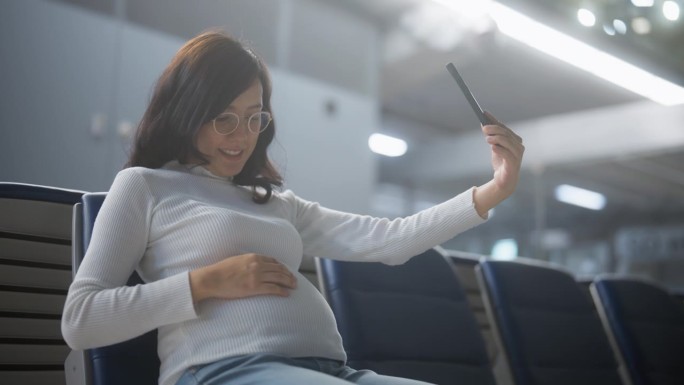 怀孕的旅客坐在机场用她的手机进行视频通话