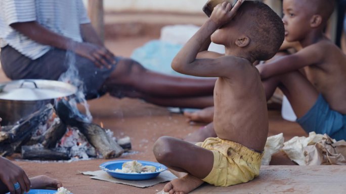 由于极度贫困、干旱和气候变化，贫穷、营养不良的非洲黑人儿童。从锅里喝水