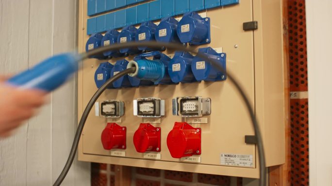 电气面板与蓝色16A和红色32A三相连接器和配电箱。技术人员将两条16A电缆连接到不同排的插座上。