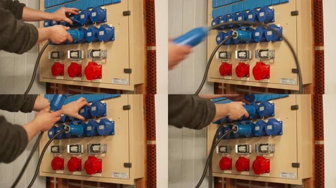 电气面板与蓝色16A和红色32A三相连接器和配电箱。技术人员将两条16A电缆连接到不同排的插座上。