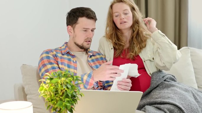 一对夫妇从收据中输入费用到笔记本电脑上的财务应用程序中。这家人要生孩子了。孕妇在网上购买商品或服务时