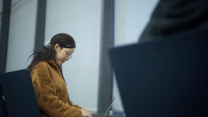 穿着黄色夹克的孕妇坐在机场用笔记本电脑工作