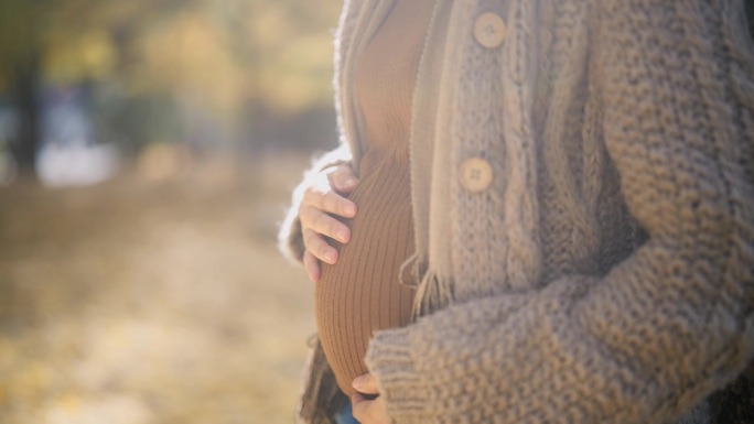 幸福的孕妇站在公园里捂着肚子的特写。