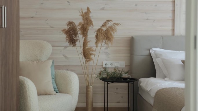 近距离舒适的卧室，柔软的椅子，床，温暖的灯在木墙上。潘帕斯草原的草在高高的花瓶里作为室内装饰，舒适的
