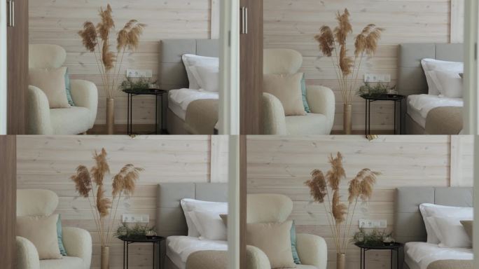 近距离舒适的卧室，柔软的椅子，床，温暖的灯在木墙上。潘帕斯草原的草在高高的花瓶里作为室内装饰，舒适的