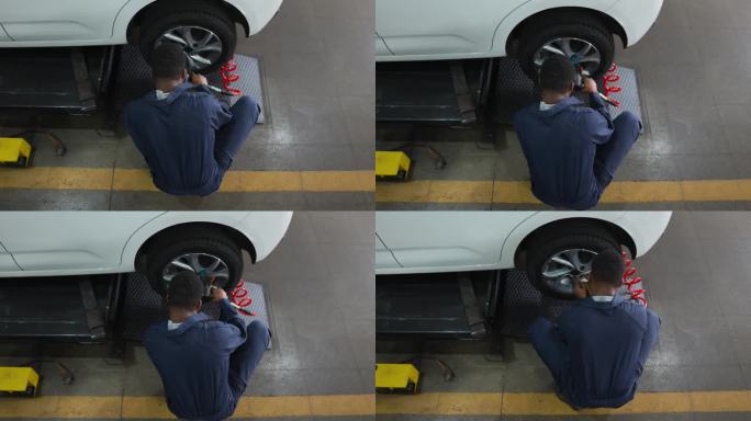 在一家汽车修理店，一名黑人男修理工正在把漏气的轮胎从车上卸下来修理