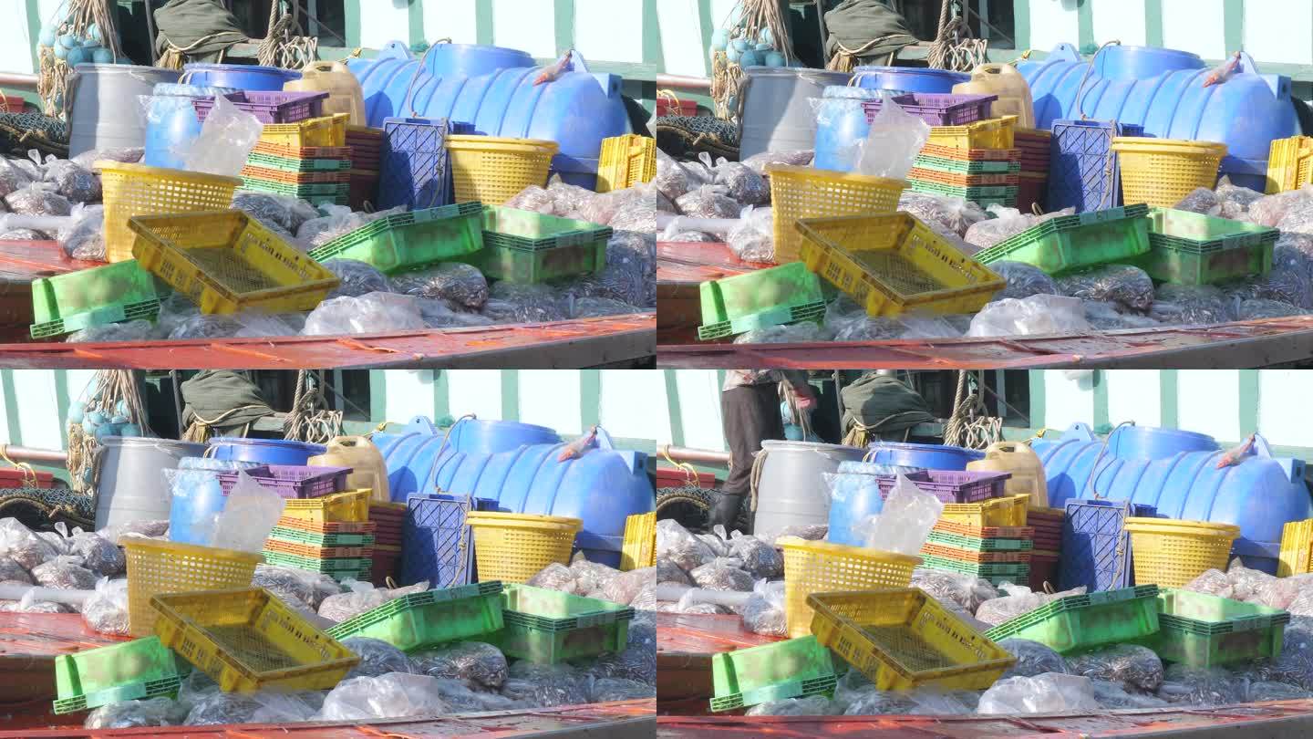 一艘上下浮动的渔船停靠在渔港，甲板上堆满了装着鱼的塑料袋、板条箱和篮子