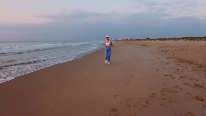 一位年轻的运动女性，有着强健的身体，在夕阳的海景下，对跑步和慢跑训练后的成绩感到满意，她很高兴。高质