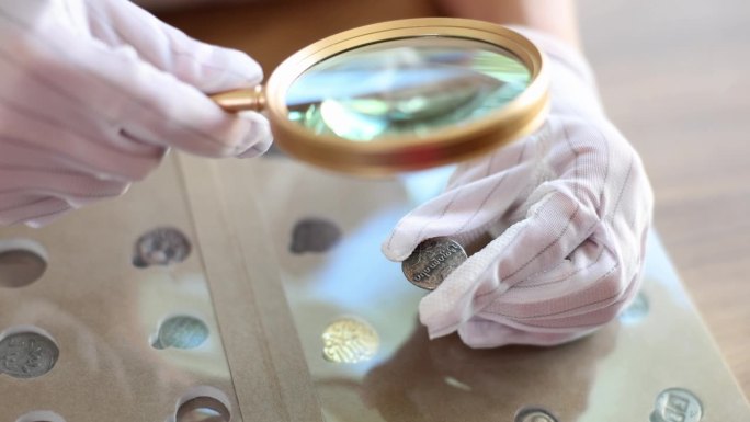 戴着手套的钱币学家通过放大镜检查收藏的硬币