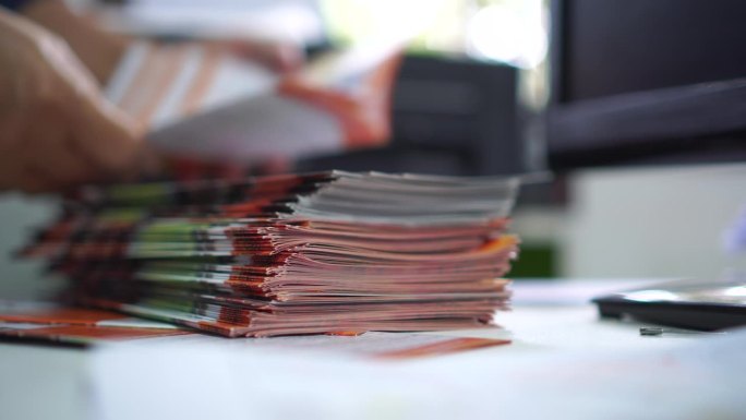 商务文件概念:商务人士在繁忙的办公室办公桌上，用手在书堆、小册子、纸质文件中检查文件、完成报告