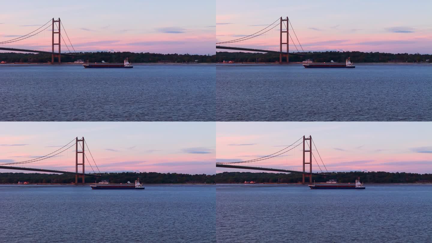 在这个迷人的无人机视频中，见证亨伯大桥下的驳船宁静的通道。这条河在夕阳温暖的怀抱下闪闪发光