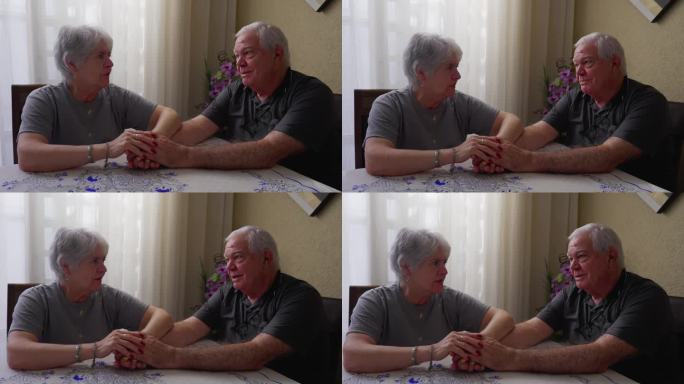 浪漫的老年夫妇在亲密的分享时刻牵着手。年迈的夫妻在家里面面相觑