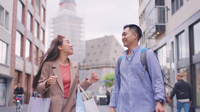 亚洲青年男女在百货公司户外购物。迷人的情侣提着购物袋，幸福地走在一起，在商场商场中心享受购物。