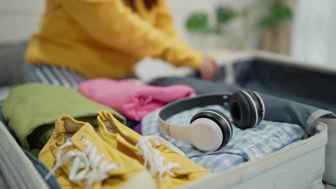 女旅客准备旅行，把衣服装进行李箱。旅行妇女把耳机和衣服装进旅行箱，准备度假旅行。旅游度假理念