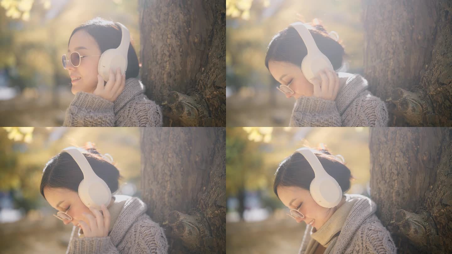 一位孕妇戴着白色耳机听音乐。秋天，她站在公园的一棵树下。