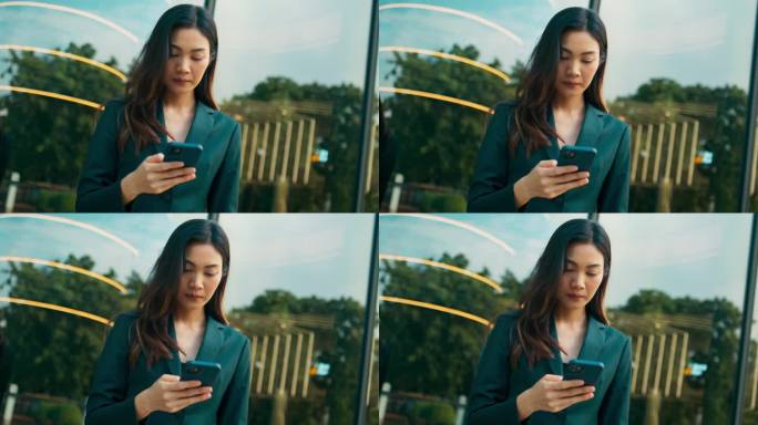 年轻漂亮的亚洲女商人使用手机，玩社交媒体，通过在线消息与人聊天，在休息时间站在户外办公室，商务人士与