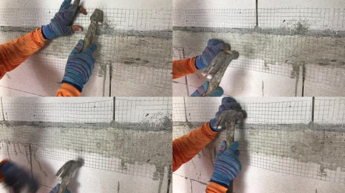 建筑工人在给轻质砖墙抹灰之前，正在把钉子钉进钢网。
