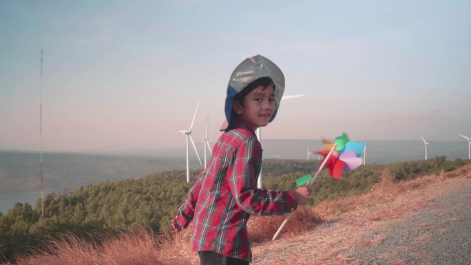 快乐的男孩在风力涡轮机旁玩风车。