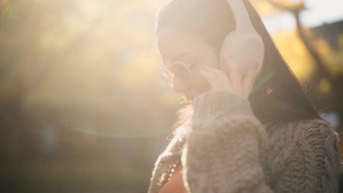 一位孕妇在自然公园放松，戴着耳机为宝宝听音乐。