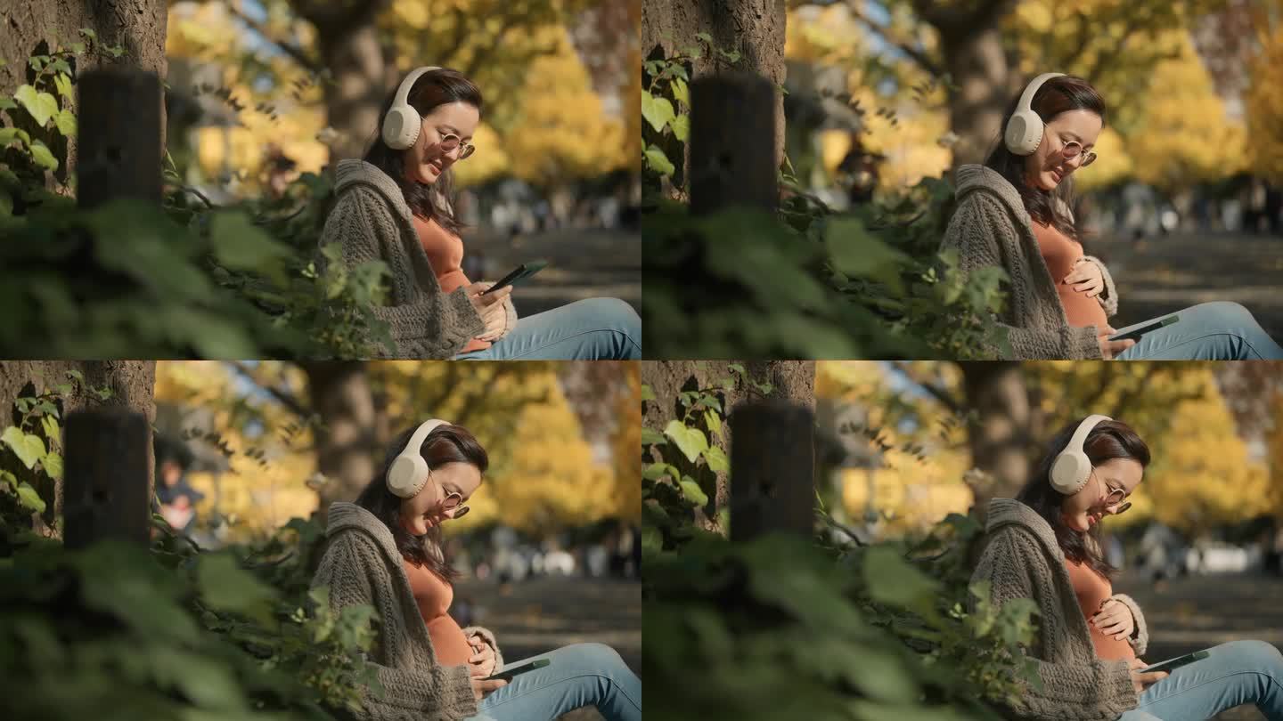孕妇坐在公园里，在树下放松，看着落叶，听音乐。