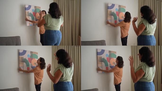 年轻女子帮丈夫在新房客厅的墙上装画框