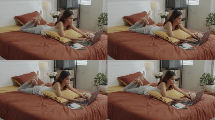 年轻的亚洲女性在床上用笔记本电脑做工作报告