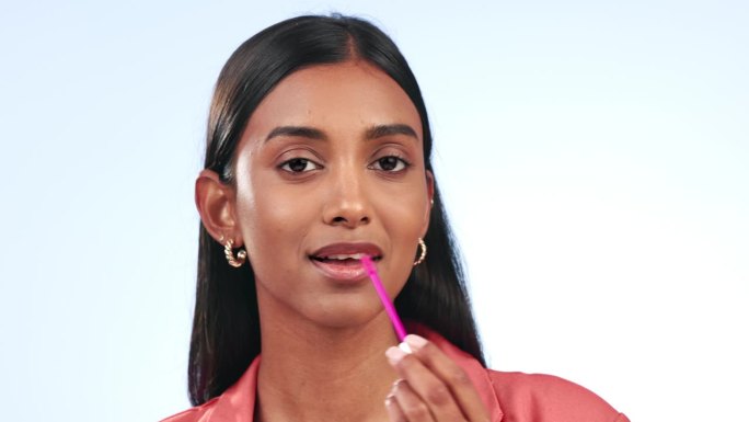 印度女人，肖像中的口红和美女，在白色背景上用化妆品发光产品刷唇。在工作室用唇彩棒为模特擦光、美容和面
