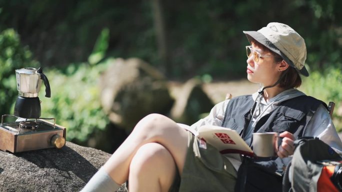 周末早上在河边露营，享受咖啡读书的亚洲华裔年轻女子