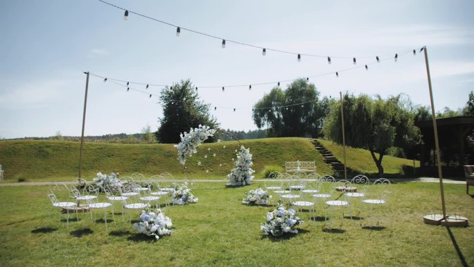 婚礼拱门以质朴的风格装饰着白色和蓝色的花朵，悬挂着灯泡灯，草坪上点着蜡烛。手持慢镜头